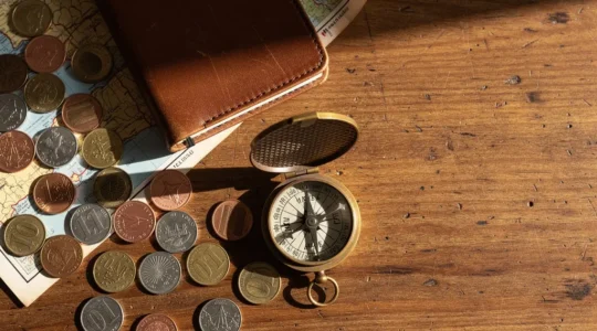 Vue en plongée d'une table de voyageur avec cartes, pièces de monnaie de différents pays et carnet de budget